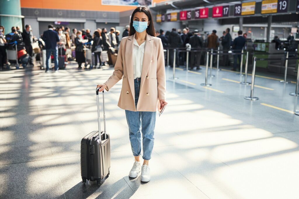 Elegant woman with travel suitcase standing at airport