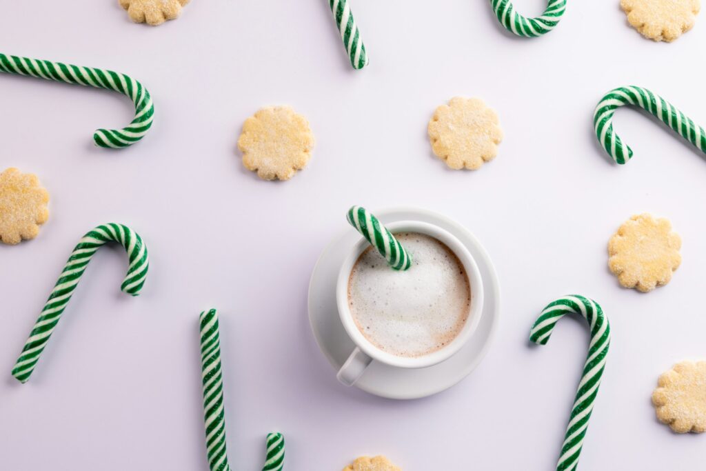 Green christmas canes, christmas cookies and cup of coffee over white background